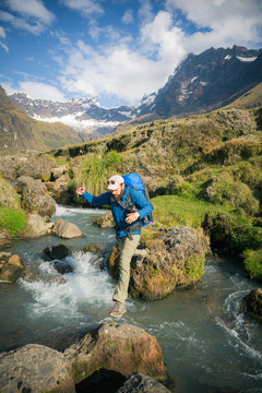 Man jumping over rocks in stream, snowcapped mountains in background, Ecuador, South America