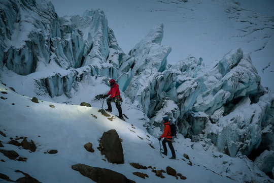 Two people ascending snow covered hillside by rock peaks, Ecuador, South America