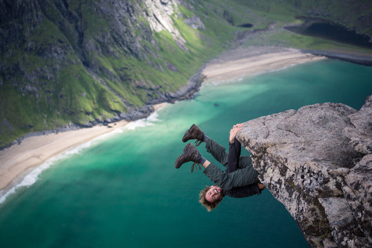 Rock climber hanging upside down off rock over bay in Norway
