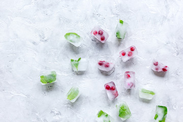 Obraz na płótnie Canvas ice cubes with red berries and mint top view gray stone background mockup