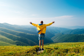 Man in yellow raincoat, jeans shorts standing at top of Carpathian mountains with view of peaks at horizon. Landscape. Nature. Valley. Travel. Freedom. Vacation. Hills. Success. Contemplation. Flight