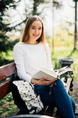 Obraz premium The student girl sitting on a bench, reading a book