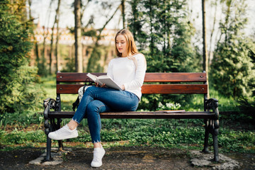 The student girl sitting on a bench, reading a book in park