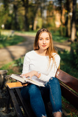 college student girl reading a book sitting on bench in city park