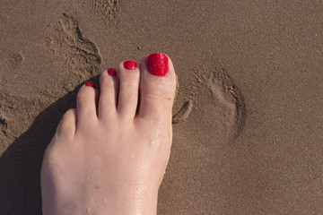 Feet of woman with nails painted red on the sand of the sea