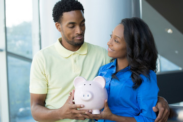 Closeup portrait, happy handsome couple or two business people holding pink piggy bank looking at each other, smiling. Smart financial decisions