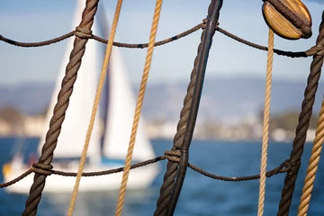 Photo sur Plexiglas Naviguer Nautical background. Close up of sailboat ropes, cables and wood pulley in grid pattern. Blurred white sailboat and blue water in the background.