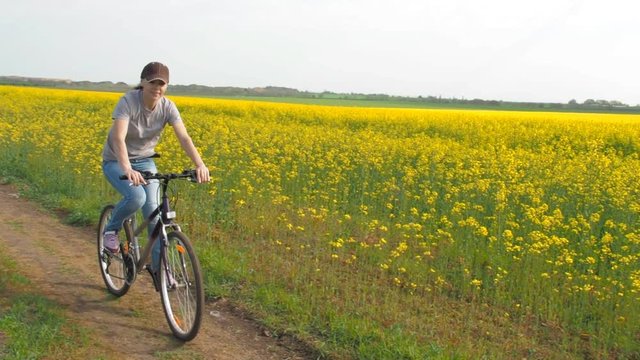 Girl on a bicycle in the nature. A woman is riding a bicycle outside the city. Healthy lifestyle. Rapeseed field. Country road. Slow motion.