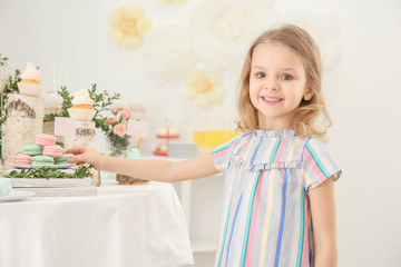 Cute girl near table with sweets served for party