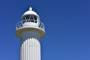Top part of white lighthouse showing circular railing and glass panes protecting light source.