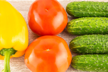 Tomatoes, yellow bell pepper and cucumber on light natural wooden background.