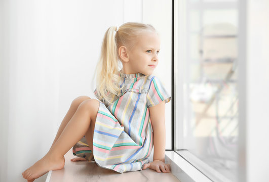 Cute little girl sitting on windowsill