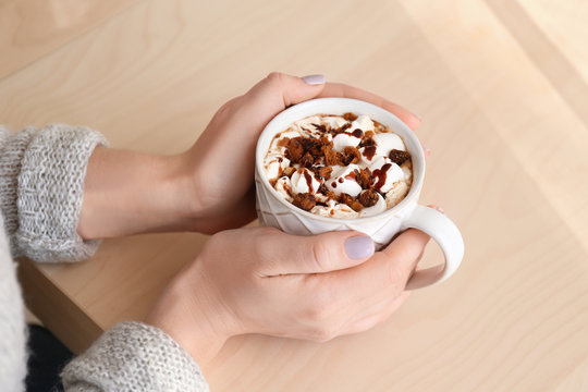 Hands of young woman and cup of tasty cocoa drink on wooden table