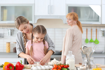 Young woman, her daughter and mother cooking in kitchen
