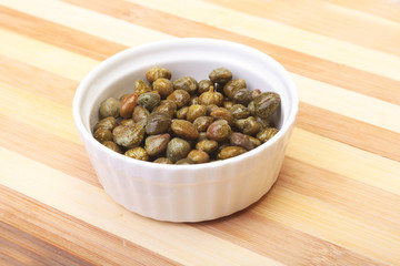 bowl with fresh capers on wooden table