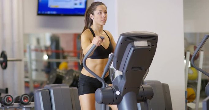 Focused woman training on ellipse exercise machine in fitness gym