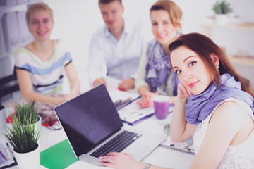 Portrait of attractive female designer sitting on desk in office