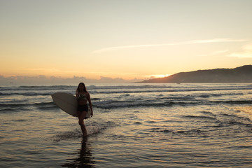 Female surfer leaving the ocean with surfboard at sunset or sunrise