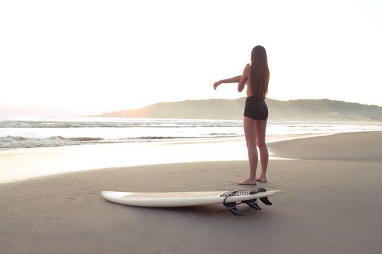 Female surfer warming up and stretching at the beach before entering ocean at sunset or sunrise