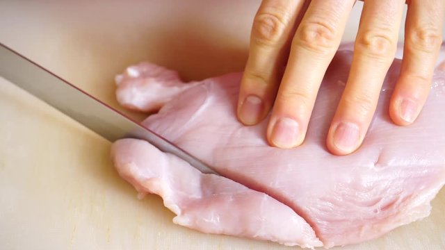 Food preparing, cooking concept. Female hands cutting slicing raw turkey meat breast on board close up 4K ProRes HQ codec