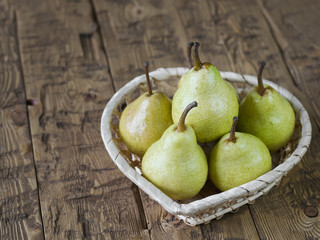Green pears in basket on rustic brown wooden table.