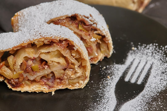 Apple strudel with icing sugar and raisins on black plate
