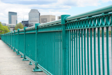perspective view of railing on river bank in city with downtown skyline