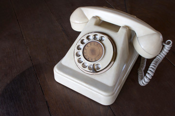 Old white phone with dust, circle dialpad and scratches on wooden retro desk. Vintage desk telephone concept.