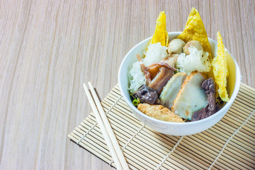 Pink seafood flat noodles (Tom Yum Yen-Ta-Fo) with fish ball and dumpling fish, special homemade red sauce serve in white bowl on wooden table