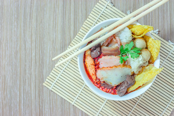 Pink seafood flat noodles (Tom Yum Yen-Ta-Fo) with fish ball and dumpling fish, special homemade red sauce serve in white bowl on wooden table, Top view