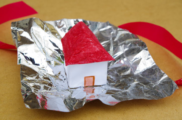 A small and beautiful house model concept over Aluminum foil with a red tie behind