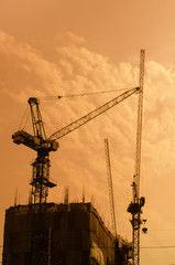 Industrial construction cranes and building silhouettes over sun at sunrise.