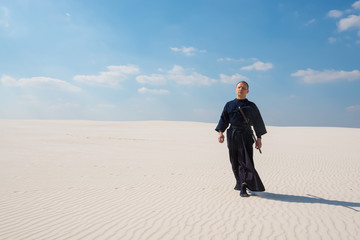 Resolute man with sword in traditional Japanese clothes goes along desert