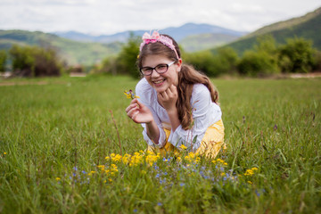 Fototapeta premium Beautiful blonde girl sitting on a beautiful green grass full of flowers and enjoy while viewing the flowers and says bouquet, sun, nature, pleasure