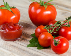 Composition from a tomato and ketchup on a wooden background.