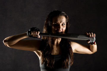 sexy athletic woman with baseball bat on dark background in the beam of a searchlight