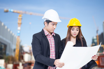 Young asian architect man and woman with blueprint in hand, outdoor construction concept, 20-30 year old.