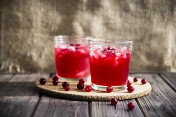 Cranberry mors with ice and berries. On a wooden table and a round cork stand © svitlini