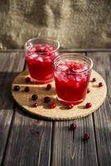 Cranberry mors with ice and berries. On a wooden table and a round cork stand © svitlini