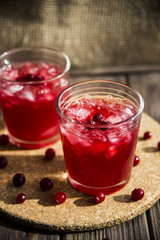 Cranberry mors with ice and berries. On a wooden table and a round cork stand