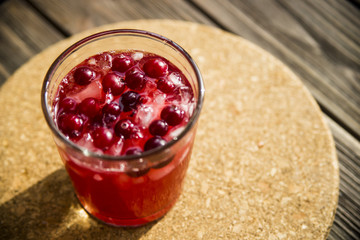 Cranberry mors with ice and berries. On a wooden table and a round cork stand © svitlini