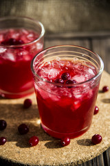 Cranberry mors with ice and berries. On a wooden table and a round cork stand © svitlini