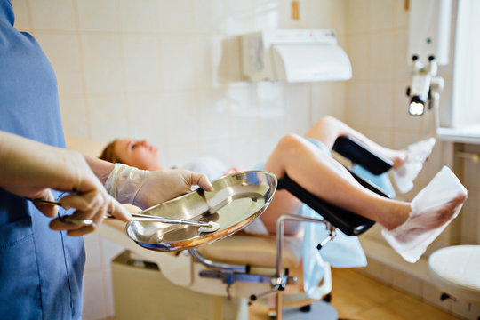 Unrecognizable female doctor holding tool in steel basin in front of the female patient on gynecological chair.