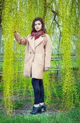 Beautiful teen girl, wearing trendy oversize beige coat and colorful scarf, standing in a spring...