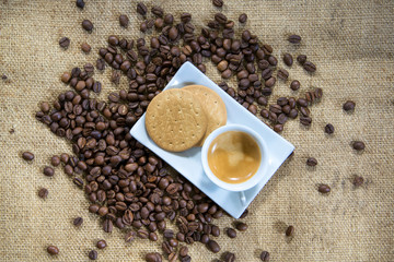 Cup of Coffee With Biscuits and Scattered Coffee Beans on Rustic Textile Background.