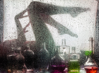 Legs of a beautiful naked girl behind a wet glass and with a still-life from bottles and wine glasses.