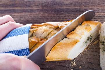 Cutting fresh bread on wooden board wrapped in towel