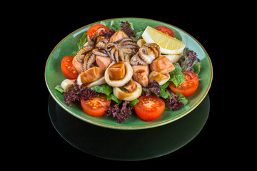 Seafood salad with octopus, shrimps, squid and vegetable on a green plate. On a black background with reflection