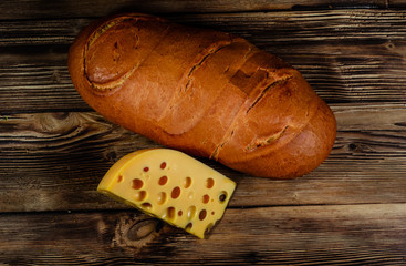 Loaf of bread and piece of cheese on wooden table. Top view