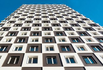 From below shot of modern and new apartment building. Photo of a tall block of flats against a blue sky.